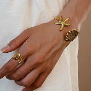 Detail of gold starfish and seashell open bangle and ring set on model wrist
