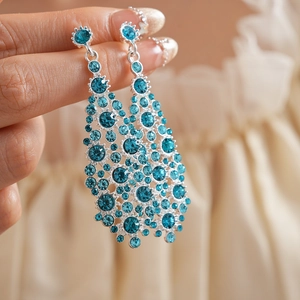 Detalle de pendientes de plata con pedrería azul sostenidos a mano para exhibición