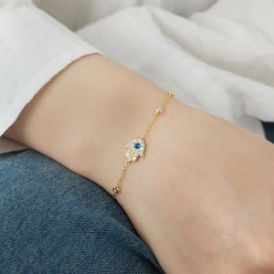 Close-up of golden Hamsa hand bracelet featuring blue gemstone and clear crystals