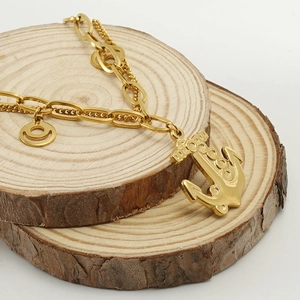 Golden double-layer stainless steel anchor bracelet with textured round charm on wood