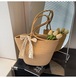 Close-up of beige woven tote bag featuring a white lace bow and straw texture detail