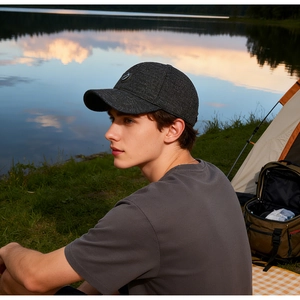 Gros plan d'une casquette gris foncé texturée avec badge au bord du lac au coucher du soleil