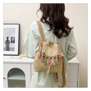 Detail of straw bucket backpack with colorful tassels and fabric strap worn by model