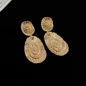 Macro shot of gold oval earrings with detailed spiral shell texture on black background