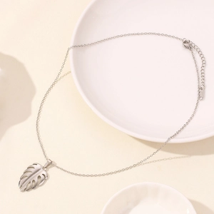 Macro shot of silver monstera leaf pendant with hollow texture on stainless steel chain