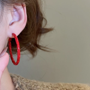 Detail of red textured geometric hoop earrings worn by a model against a neutral background