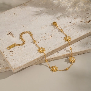 Detail of 18KGP gold flower bracelet with diamonds on a textured stone surface