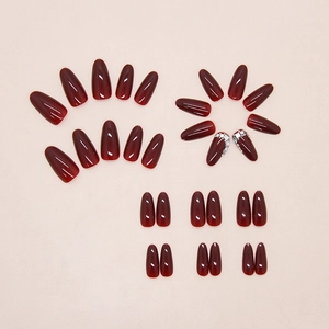 Detail of burgundy press-on nails with silver rhinestones and pearls in long almond shape