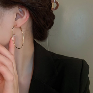 Gros plan d'élégantes créoles dorées portées par un mannequin en tailleur noir chic