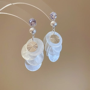Detailaufnahme von Boho-Quastenohrringen mit lila Zirkon und weißen Muschel-Anhängern