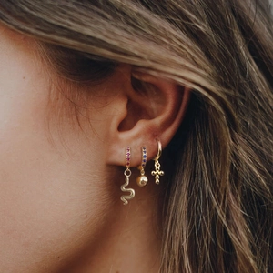 Close-up of gold hoop earrings set with snake, cross, and sphere charms on model