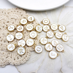 Detail of white round alloy alphabet pendants with gold plating on lace background
