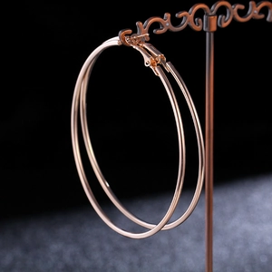 Close-up of large rose gold hoop earrings featuring a classic clasp on a vintage stand