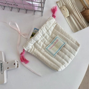 Close-up of a white quilted drawstring pouch with pink tassels and a silk bow decoration