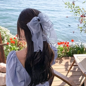 Blue large mesh bow hair clip with ribbons on long wavy hair with a scenic lake background
