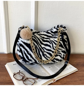 Detail of zebra pattern plush shoulder bag with chunky gold chain on a wooden desk
