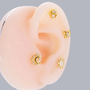 Close-up of golden stud earrings with moon butterfly and star designs on ear model
