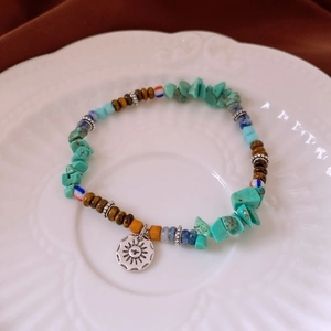 Détail d'un bracelet bohème en perles de turquoise avec un pendentif soleil en argent