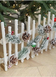 Macro detail of white wooden Christmas fence with artificial snow, pine cones and red berries
