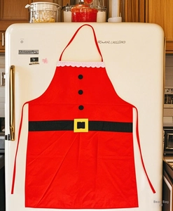 Detail of Santa Claus apron with black buttons and belt hanging on a white kitchen fridge