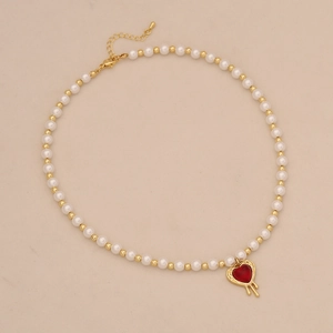Detailed view of pearl necklace with red heart pendant and gold bead accents
