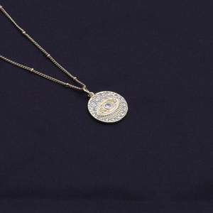 Elegant gold evil eye necklace with clear zircon stones on a dark blue fabric background