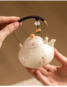 Close-up of ceramic teapot with floral motif and rope-wrapped handle held by hands