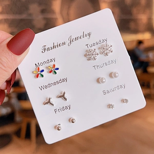 Close-up of 6 pairs of silver earrings with flower, pearl, and zircon on weekly card