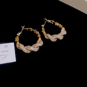Detail of twisted gold hoop earrings with sparkling white cubic zirconia on black velvet