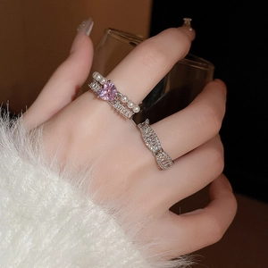 Détail de bagues superposées avec cœur en zircon, perles et accents argentés au doigt