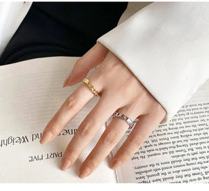 Primer plano de anillos de cadena ajustables en oro y plata usados en la mano sobre un libro