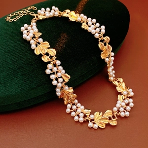 Macro shot of vintage gold floral pearl necklace with leaf charms on green velvet
