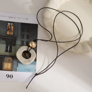 Zen style irregular beige resin pendant necklace with gold bead on black cord cord