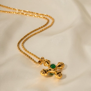 Macro detail of 18k gold plated cross pendant with green gemstone and rope chain