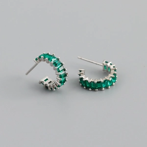 Detailed macro view of silver hoop earrings featuring emerald green rectangle zircons