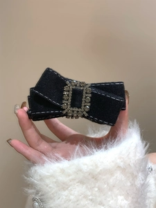 Détail d'une pince à cheveux nœud en tweed noir avec surpiqûres blanches et strass brillants