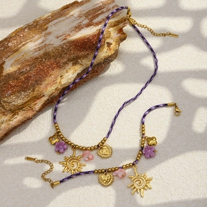 Détails du collier en corde tressée avec pendentifs soleil et cœur dorés sur une roche