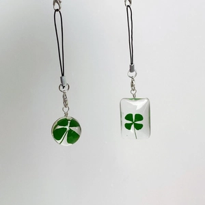 Macro shot of resin pendants with real pressed four-leaf clovers and black woven ropes