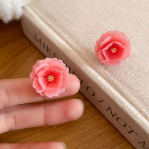 Détail de boucles d'oreilles fleur en résine rose avec pistils dorés et fini mat