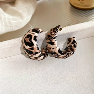Macro shot of leopard print C-shape earrings on white fabric with sharp vintage details