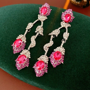 Close-up of vintage flower tassel earrings with magenta gemstones on a green velvet pad