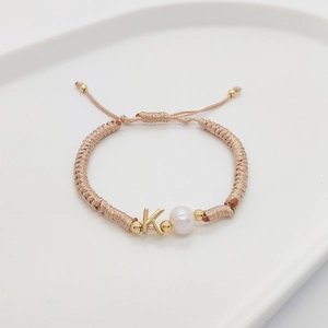 Detail of hand-woven bracelet with gold letter K charm and natural freshwater pearl