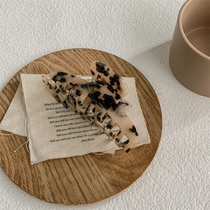 Macro detail of tortoiseshell acetate hair claw clip on rustic linen and wood coaster