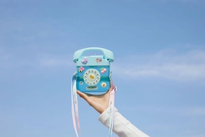 Blue retro telephone-shaped water bottle with pink strap held against the blue sky