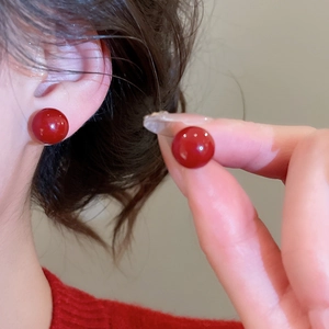 Close-up of a bright red round stud earring worn on ear to show scale and glossy finish