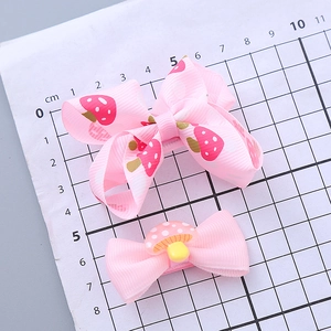 Pink handmade bow hair clips with strawberry and mushroom motifs on a measurement mat