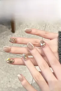 Detail of nude cat-eye press-on nails with champagne glitter and chunky metallic stone accents