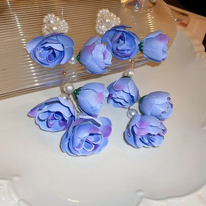 Macro shot of blue silk rose fabric earrings with elegant white pearls on a glass tray