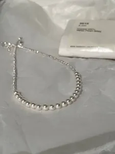 Close-up of 6mm white pearls and fine silver chain on a textured white paper background