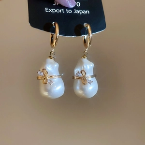 Vue détaillée de boucles d'oreilles dorées avec perles baroques et nœuds cristallins